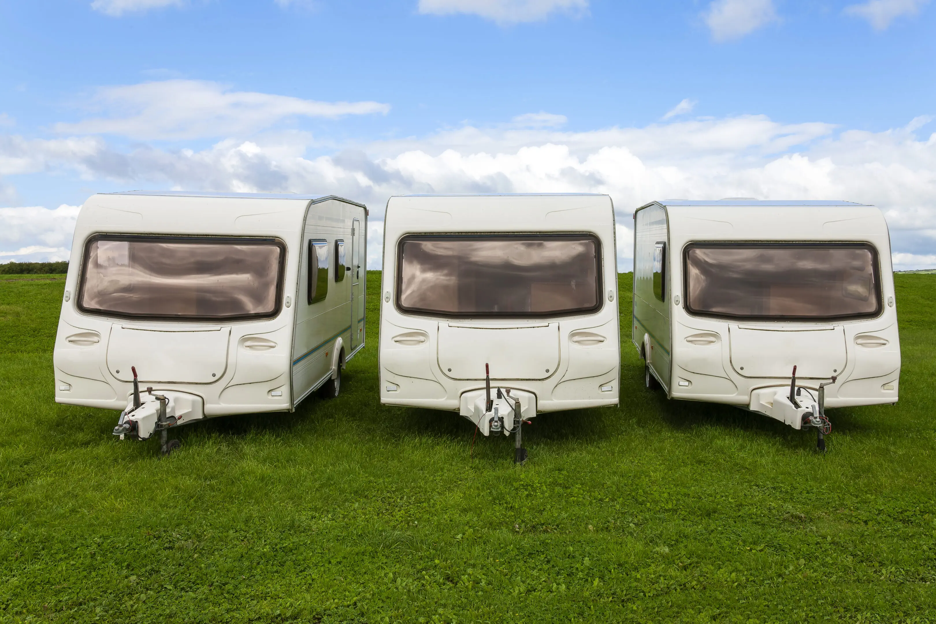 Caravan travel trailers Three white recreational vehicles parked in a row.