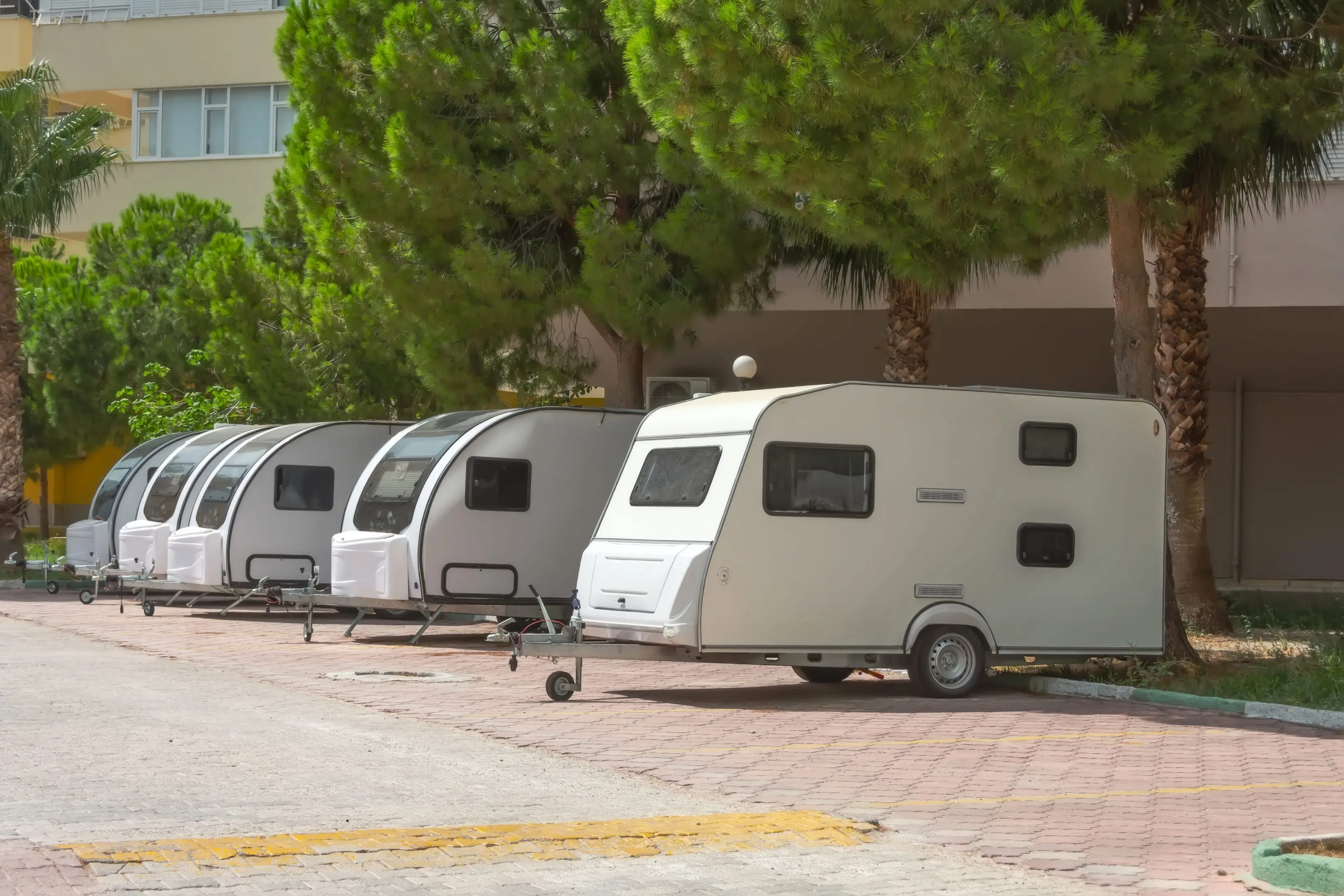 Several motorhome trailers parked in a residential area. A row of white trailers parked in front of trees.