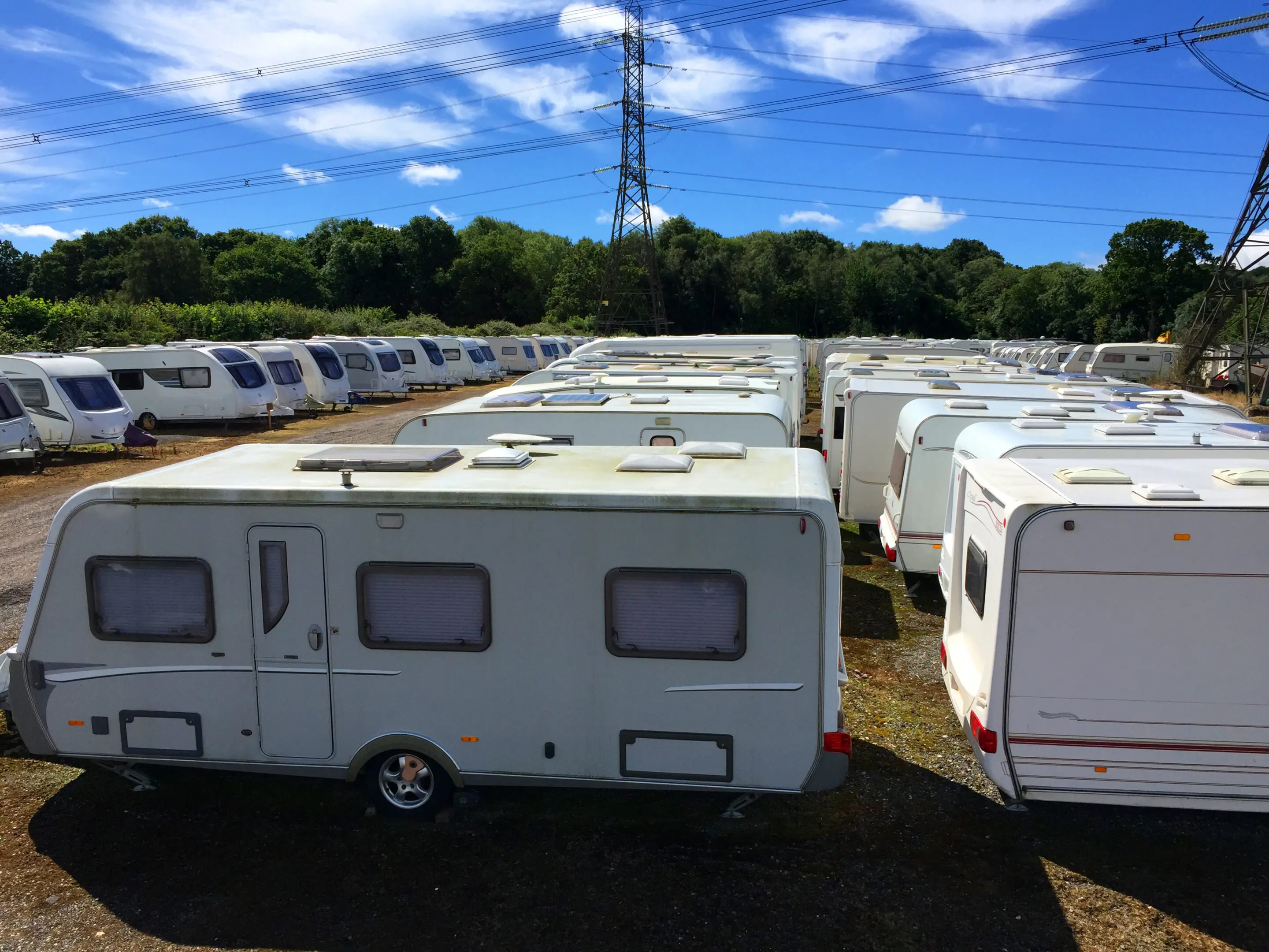 Caravans stored in rows on a sunny day. A lot of white trailers parked in the grass.